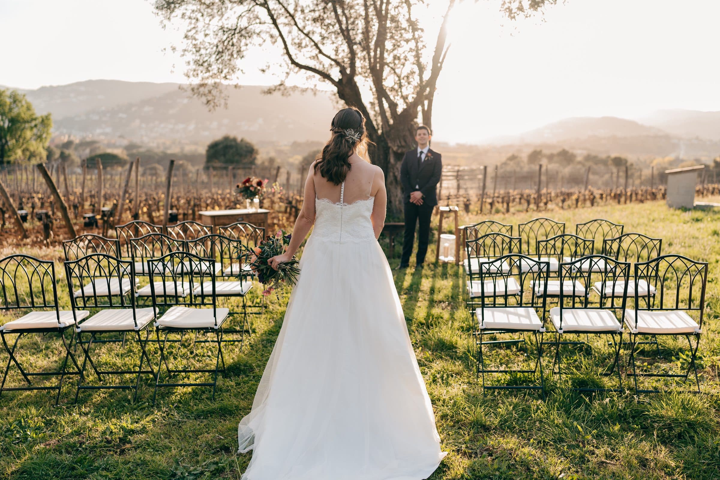 Novia caminando hacia la ceremonia entre filas de sillas en el viñedo