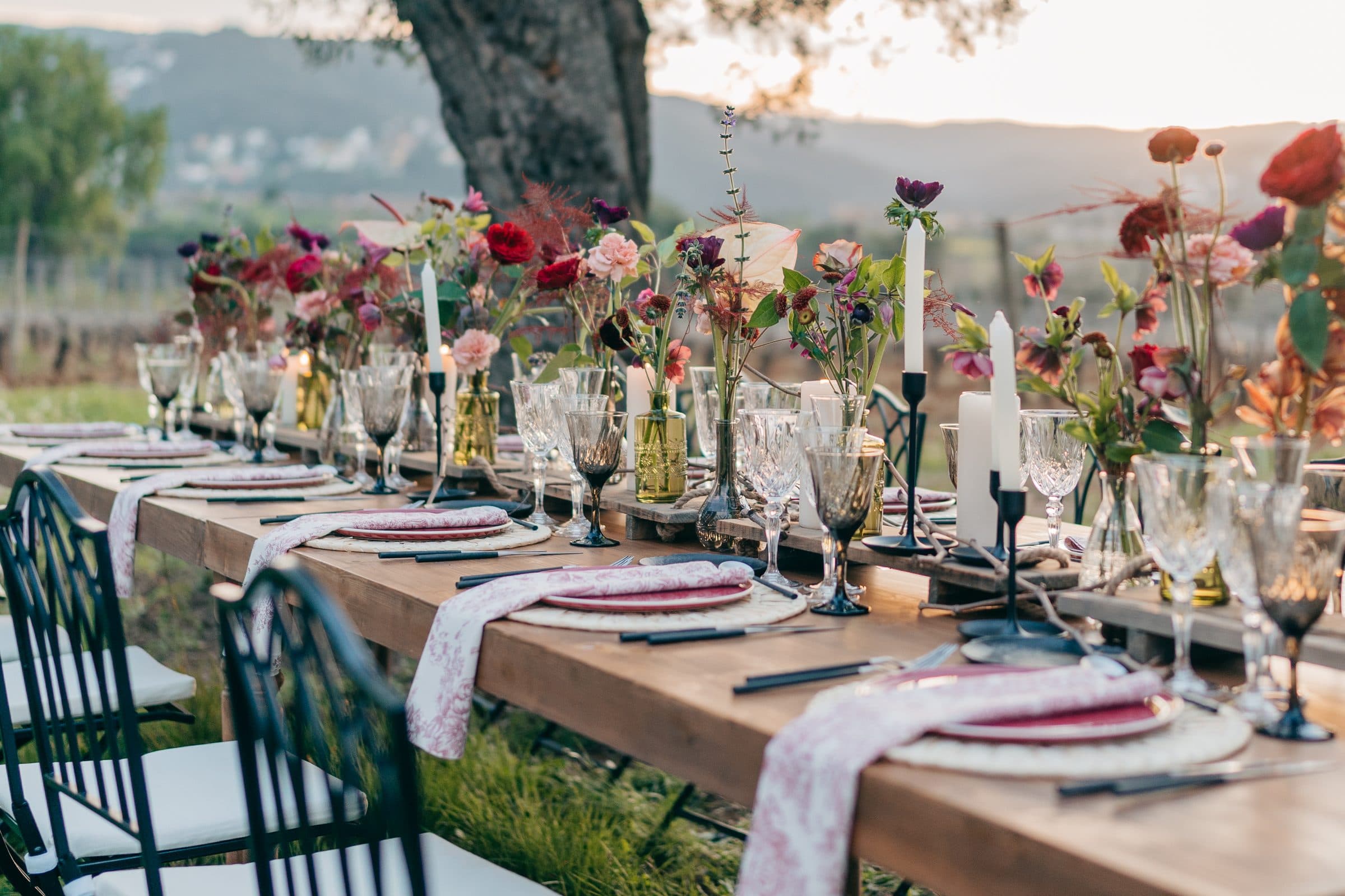 Mesa larga decorada con flores al atardecer entre las viñas