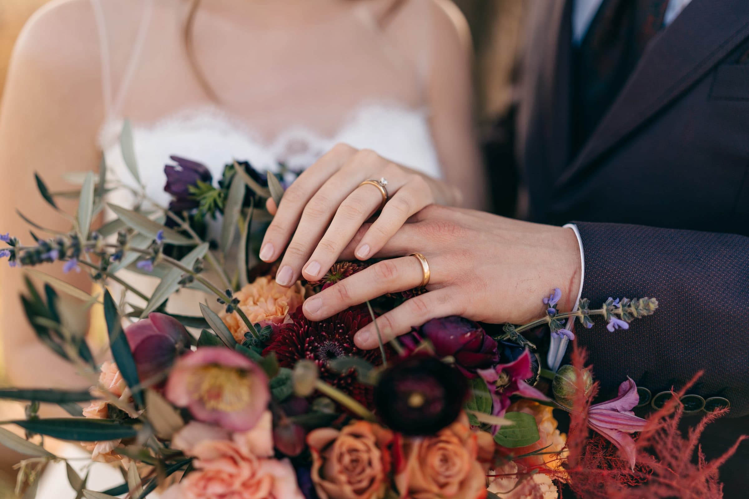Manos de los novios con los anillos sobre el ramo